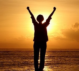 silhouette of person with arms raised against sunset background