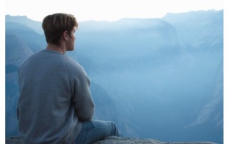 young man sitting on cliff facing away from camera