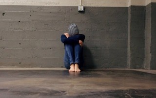 barefoot person with head on knees in empty building