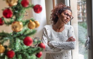 African American woman with arms crossed looking out the window at Christmas time - SAD