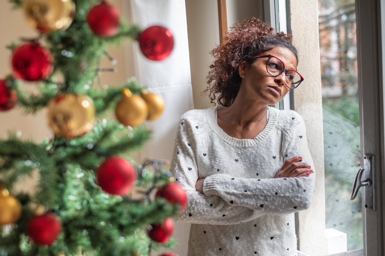 African American woman with arms crossed looking out the window at Christmas time - SAD