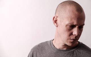 upset man with shaved head looking down - denial