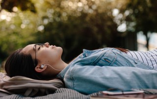 young woman lying down on blanket outside with headphones - sobriety first