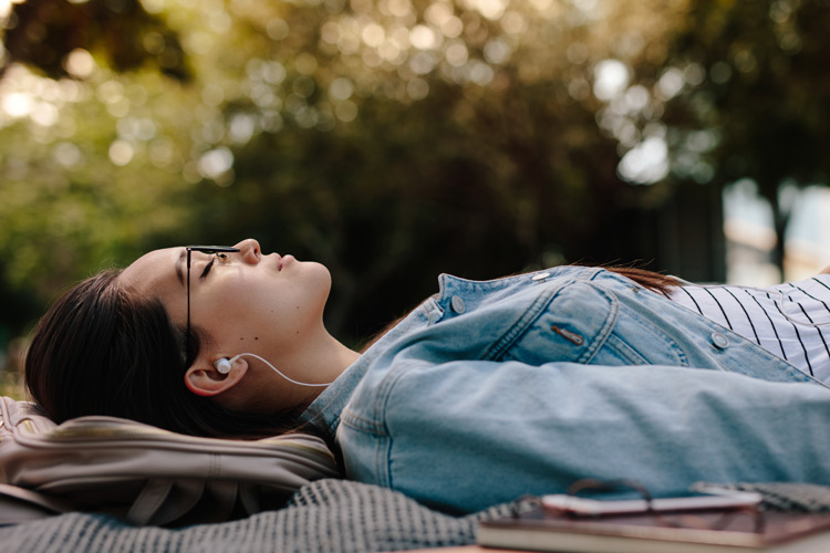 young woman lying down on blanket outside with headphones - sobriety first