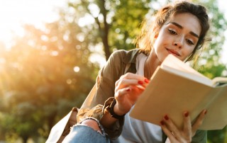 pretty young woman reading book outdoors - recovery during pandemic