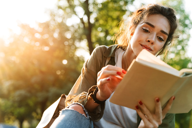 pretty young woman reading book outdoors - recovery during pandemic