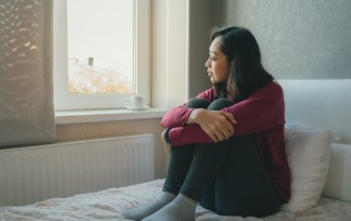 Don't Put Off Rehab, pretty Asian woman looking out window sitting on bed - put off rehab - COVID-19