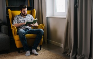 man sitting at home in yellow chair reading a book - mental health - COVID-19