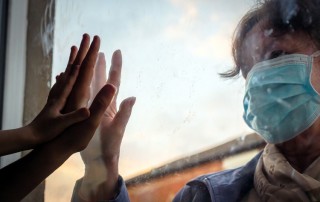 pandemic-related mental health challenges, older woman in face mask holding her hand up to child's hand on window pane - mental health and pandemic