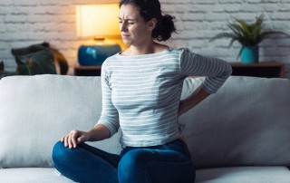 young woman sitting on couch, suffering with back pain - chronic pain