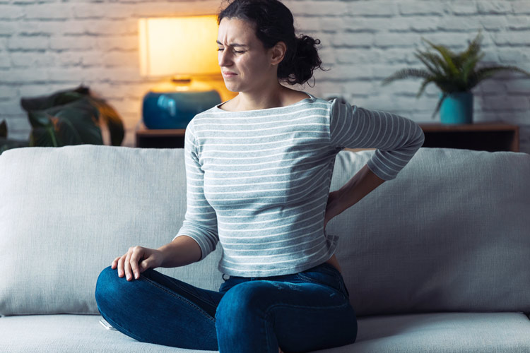 young woman sitting on couch, suffering with back pain - chronic pain