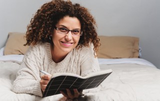 woman smiling laying on bed with journal out - writing in journal - gratitude