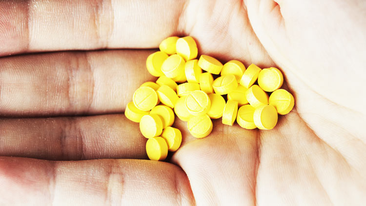 close up of a hand full of small yellow pills - Clonazepam Addiction