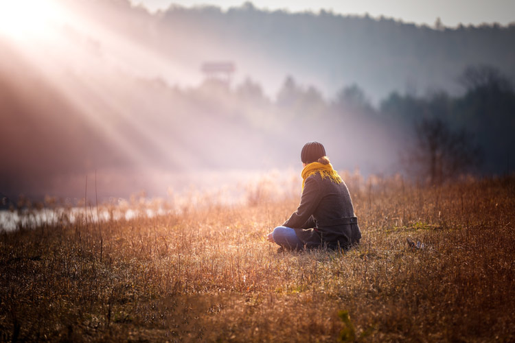 person sitting alone in field on a foggy day with rays of sun shining down upon them - mental health