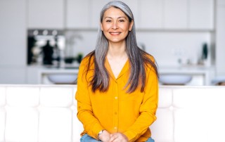 beautiful woman in her 50's smiling at the camera, wearing a bright yellow blouse in her kitchen - mindfulness practices