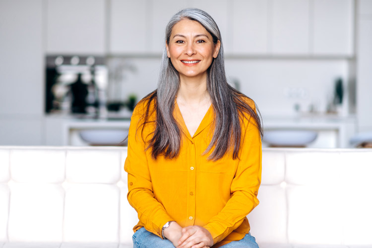 beautiful woman in her 50's smiling at the camera, wearing a bright yellow blouse in her kitchen - mindfulness practices