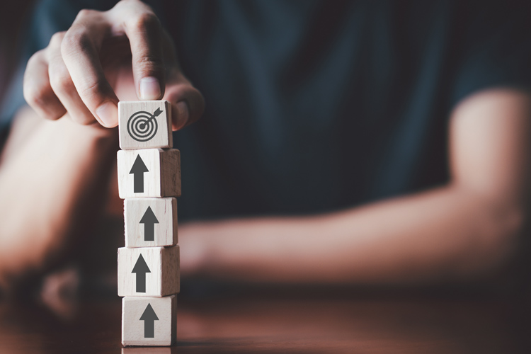 cropped shot of man stacking wooden blocks with arrows pointing upward and the top block having a target on it - goal setting