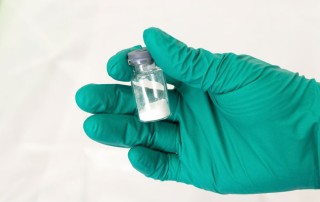 closely cropped shot of green gloved hand holding a vial of white powder - fentanyl