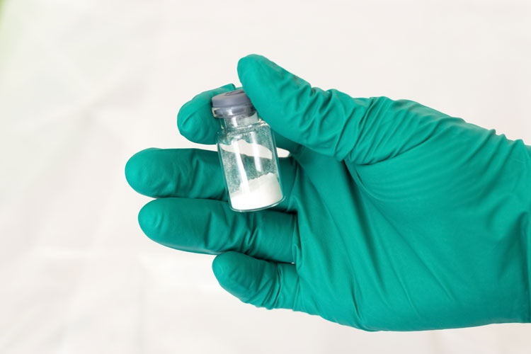 closely cropped shot of green gloved hand holding a vial of white powder - fentanyl