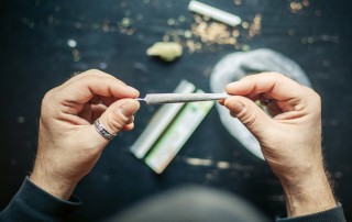 cropped shot of a man's hands holding a freshly rolled marijuana cigarette