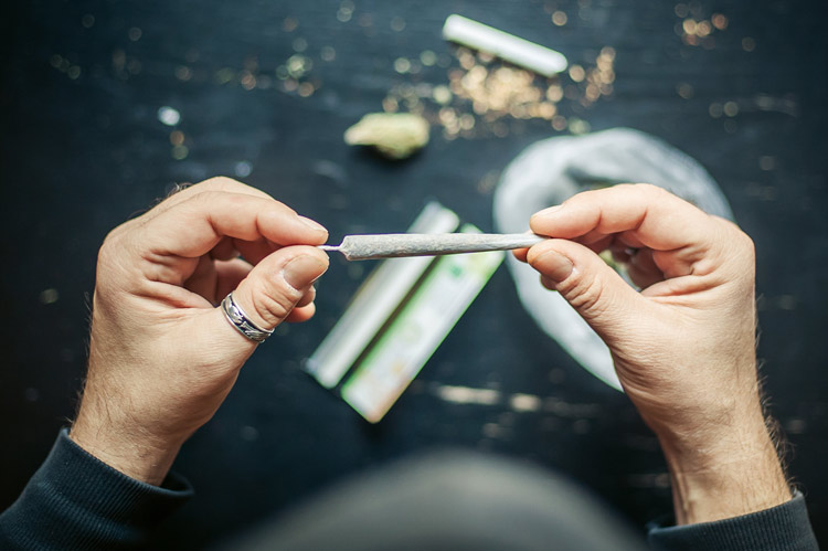 cropped shot of a man's hands holding a freshly rolled marijuana cigarette