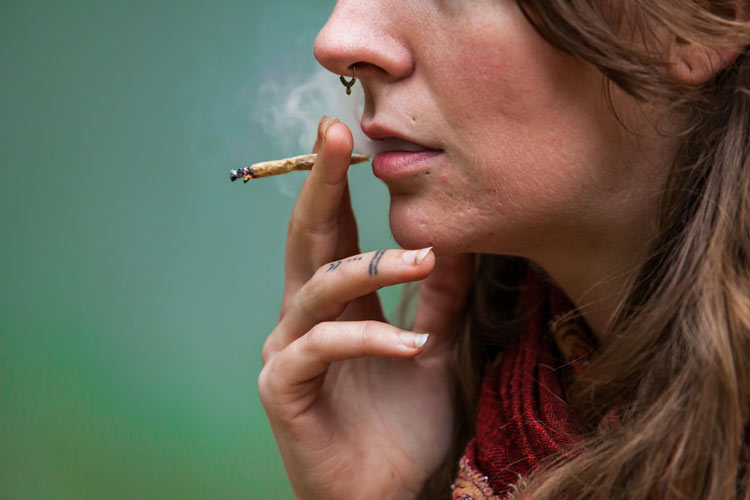 closely cropped shot of a young woman smoking a small marijuana cigarette - marijuana use