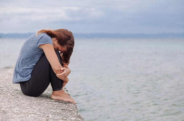 young woman at the beach with knees drawn up to her chest very distraught - suicide