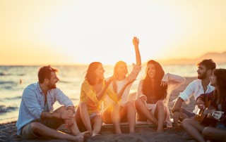 group of young adult friends at the beach having fun talking and playing guitar - summer fun