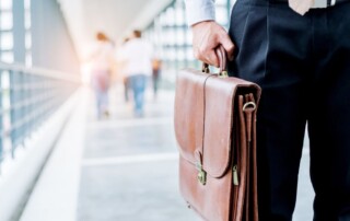 Businessperson holding a leather briefcase while walking in a modern office corridor, symbolizing professionalism, employment, or workplace issues.