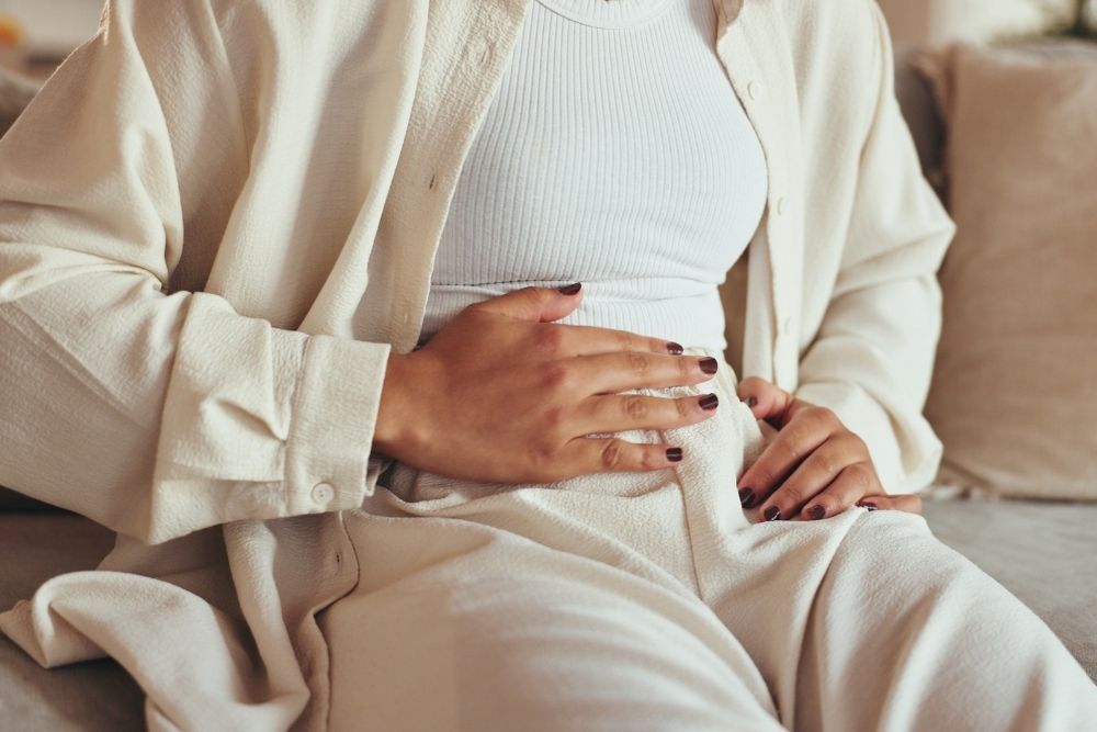 A woman sitting on a couch with her hands on her stomach, suggesting discomfort or digestive issues related to gut health.