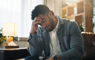A man sitting indoors with his head in his hand, appearing overwhelmed, stressed, or deep in thought.