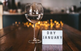 a wine glass sits on a table. A white sign with black border reads dry january in black letters.