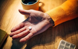 St Joseph - Will I Get Addicted to Pain Pills. An individual holds a single pill in the palm of their open hand, resting on a table.